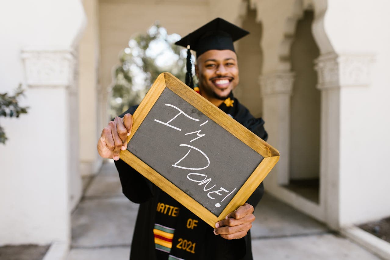 man wearing graduation regalia holding a chalkboard